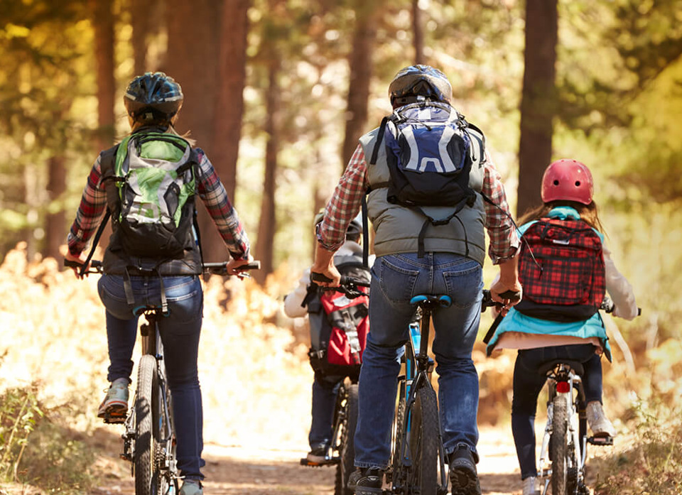 En familj med två vuxna och två barn som cyklar längs en grusväg i skogen.